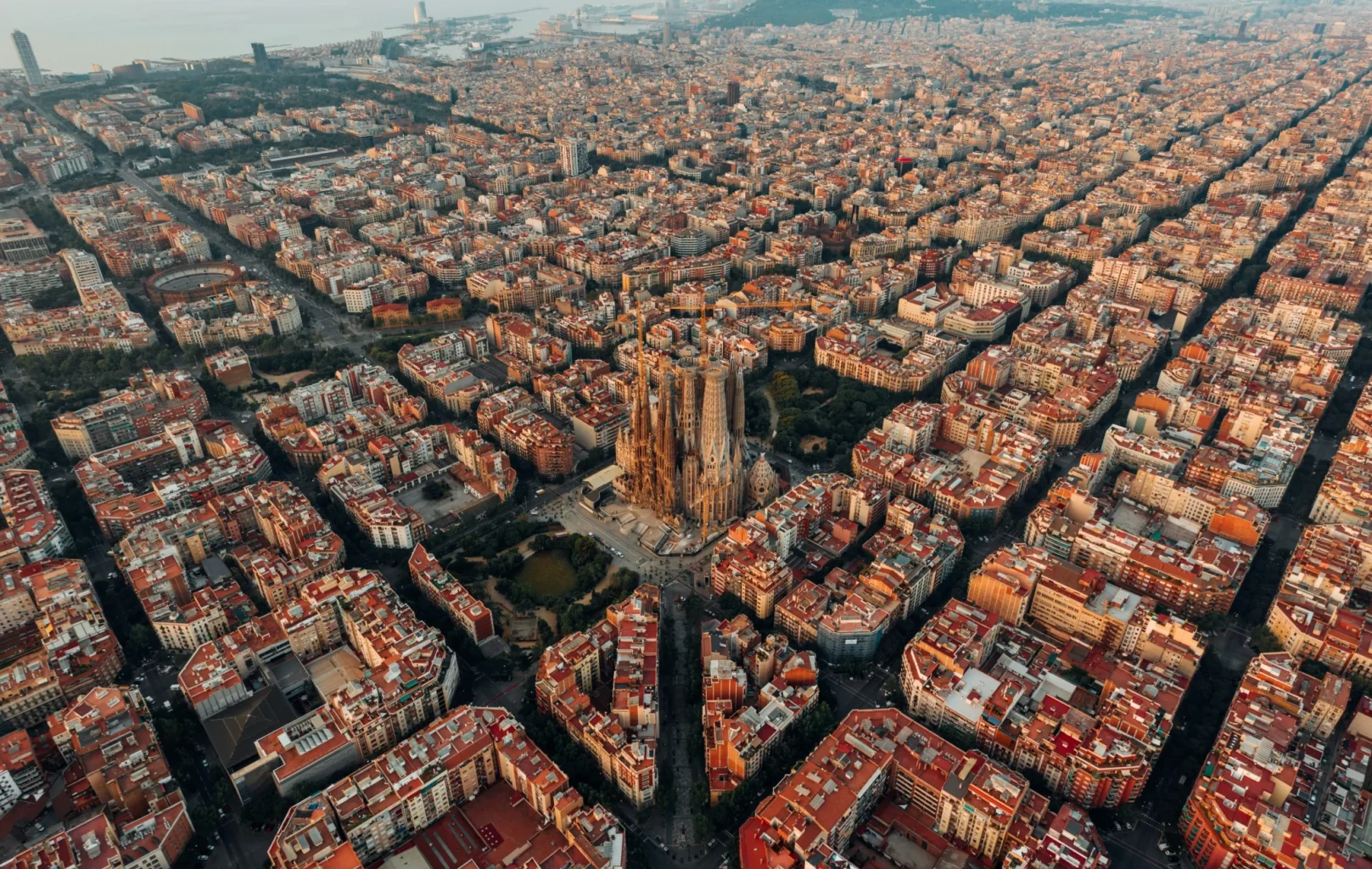 Aerial view of Barcelona’s city grid with the Sagrada Família basilica in the center, L’Auditori Barcelona nearby, all surrounded by densely packed buildings.