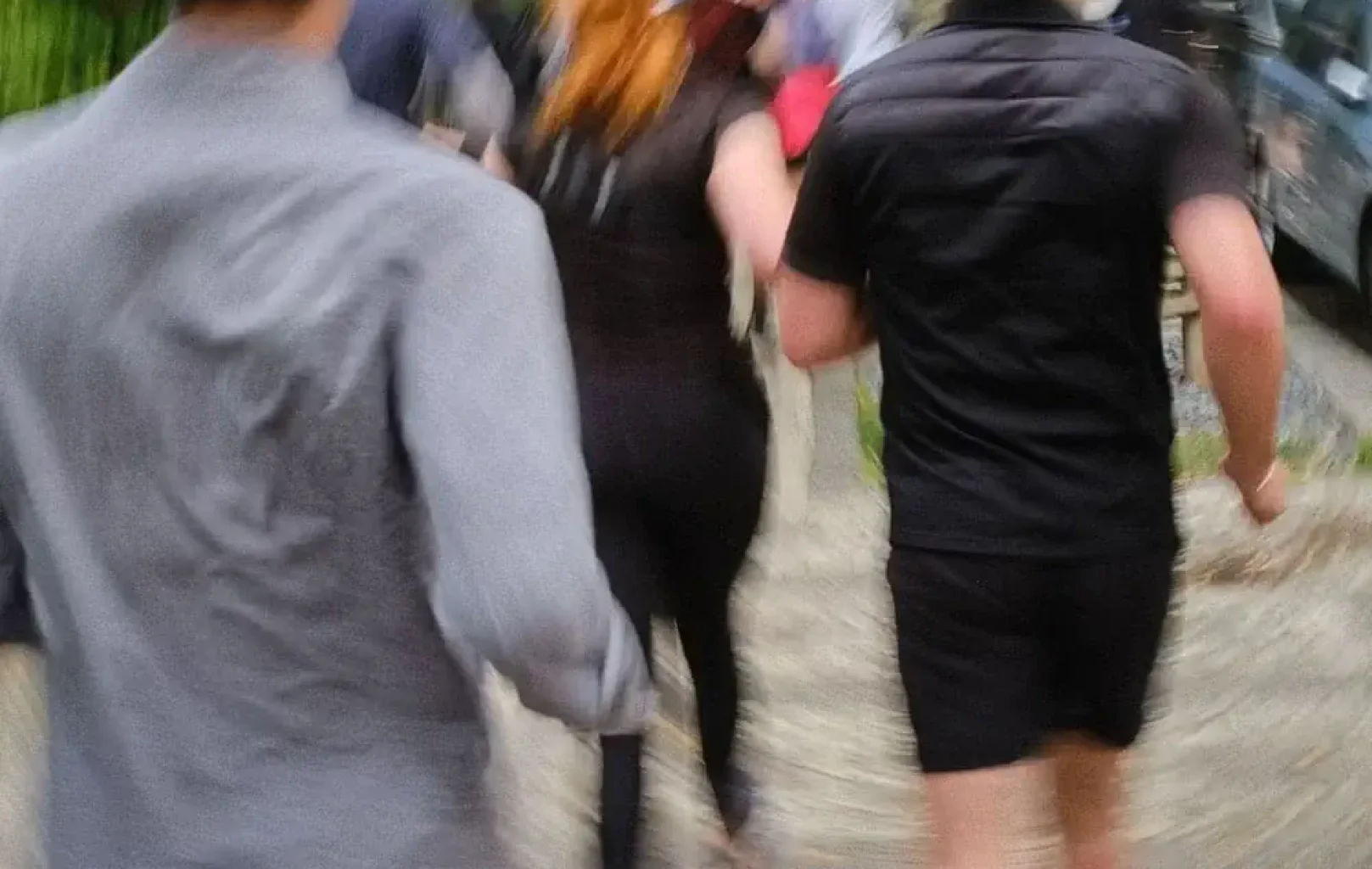 Eine Gruppe eines Laufclubs, die von hinten gezeigt wird, geht oder läuft einen Weg im Freien entlang. Das Bild ist leicht unscharf und suggeriert Bewegung - ein Moment, um sie für ihre Energie und Kameradschaft zu lieben.