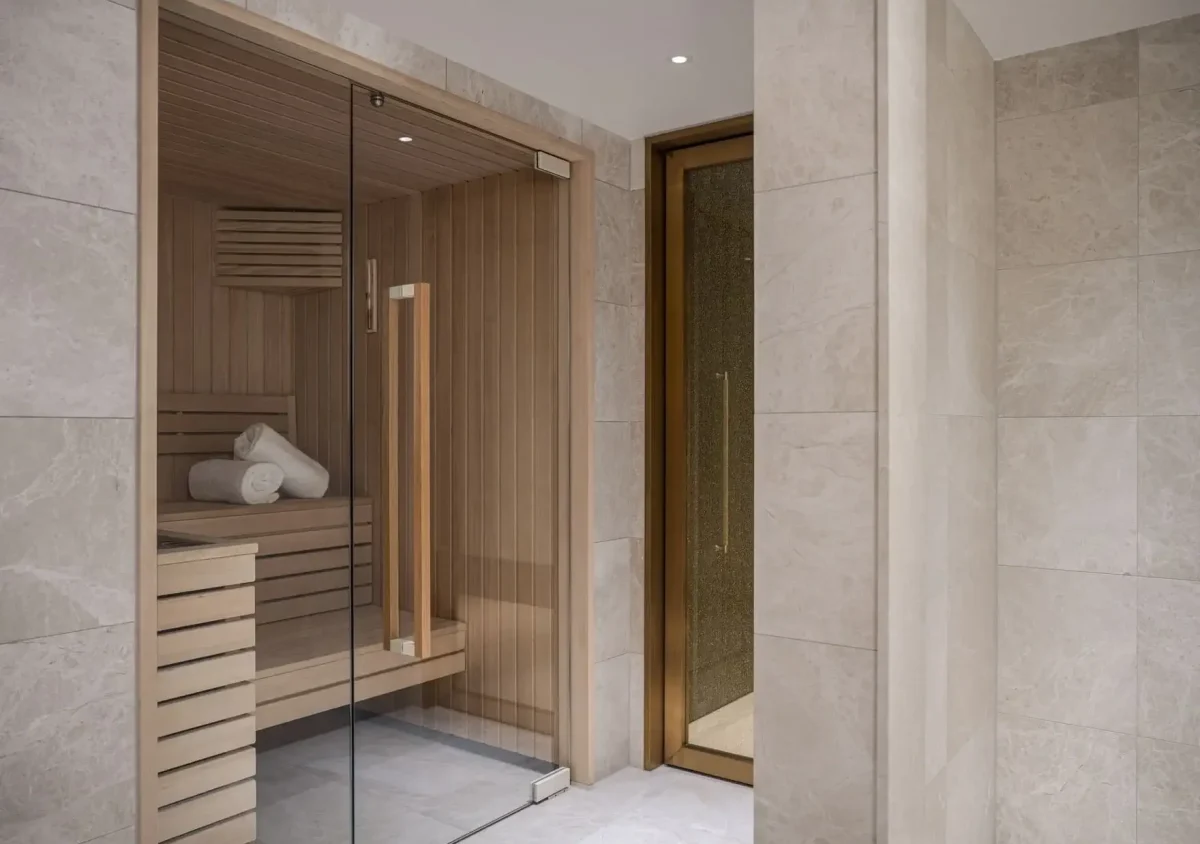 A modern sauna room with wooden benches and rolled towels, enclosed by a glass door, sits next to a tiled shower area in the luxurious Duplex Suite.