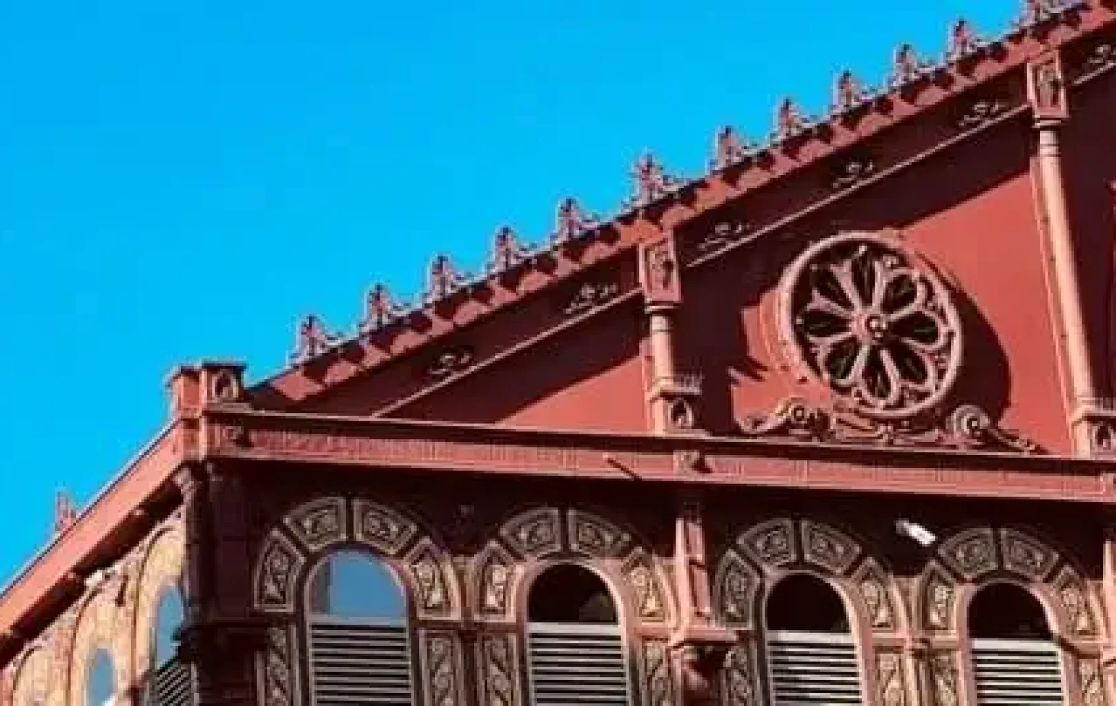 Red ornate building facade with arched windows and circular decorative detail against a clear blue sky, capturing the vibrant spirit of Barcelona—an invitation to savour the earth’s artistry.