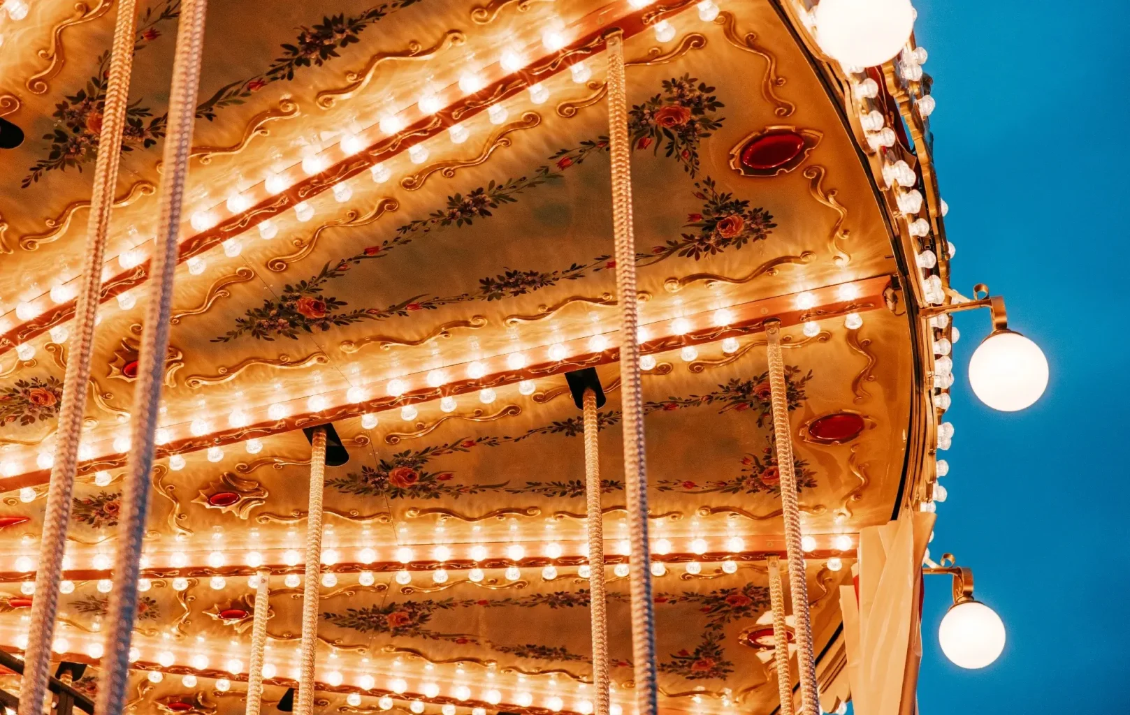 Close-up of an ornate, illuminated carousel canopy with decorative floral patterns and rows of glowing lights at Vienna’s Christmas Markets, set against a clear blue evening sky.