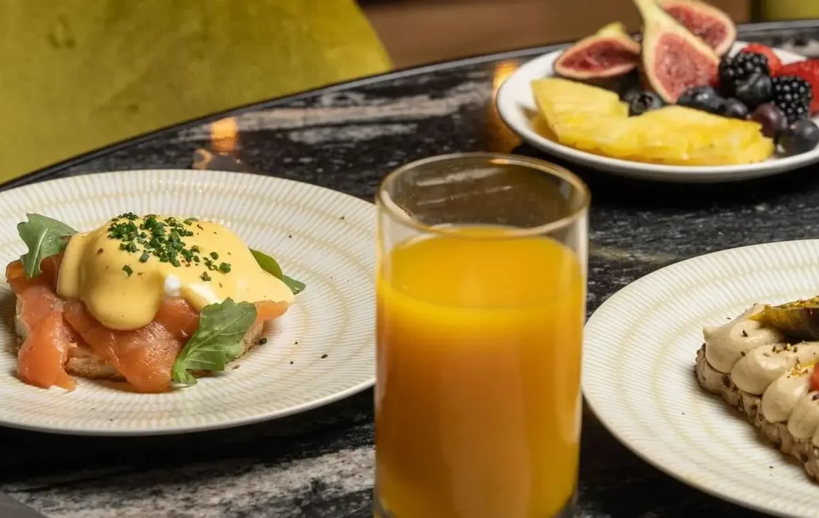 Una taula d'esmorzar amb ous Benedict, torrades amb ingredients, un got de suc de taronja, un plat de fruita i unes postres en un got: perfectes per començar la teva Escapada de Tardor.